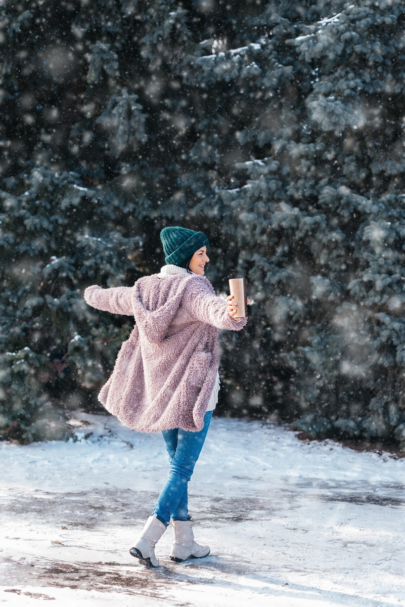 young woman walking on winter day, holding travel stainless steel mug with hot coffee. reusable water bottle.
