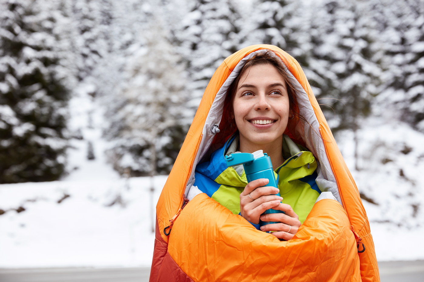 BER HUG - termo flaške, posode in lončki za vsak trenutek smiling woman traveler hikes on snowy mountain, warms in sleeping bag, drinks hot tea or coffee, poses over amazing winter lanscape, snow covered fir trees, has dreamy expression. adventure trip